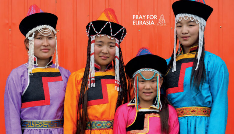 Eurasian women and children in colorful traditional costumes, standing against a vibrant orange back.