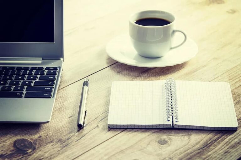 Office workspace with laptop, notebook, pen, and coffee.