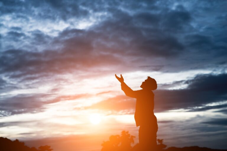 A person reaching towards the sunset with outstretched hand during dusk.