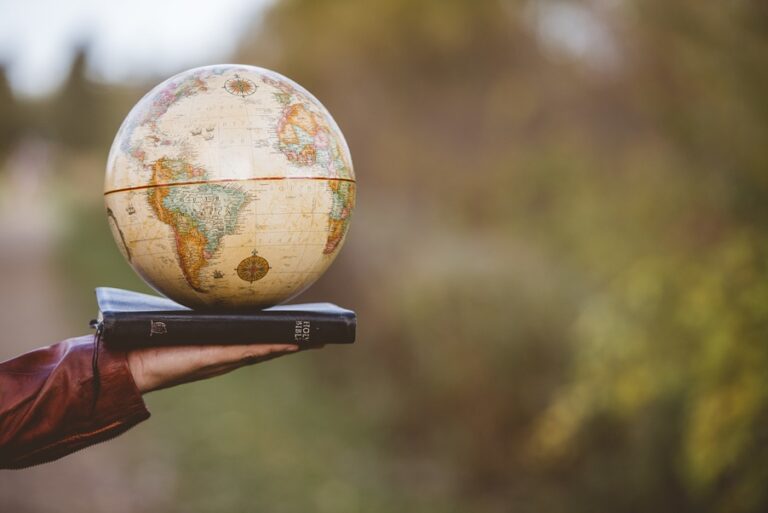 Earth globe resting on a closed book held by a person outdoors with blurred natural background.