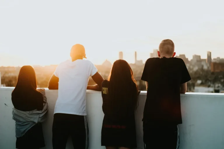 Group of diverse young adults watching sunset over city skyline from rooftop.