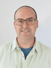 Portrait of a smiling man wearing glasses, light shirt, and blue undershirt.
