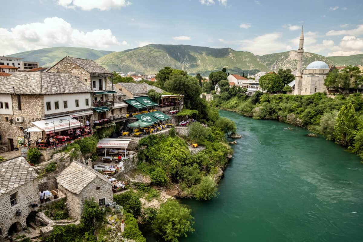 Scenic view of a riverside town with historic buildings and mountains in the background.