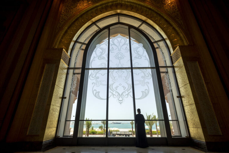 Person looking out large arched window with ocean view and decorative design.