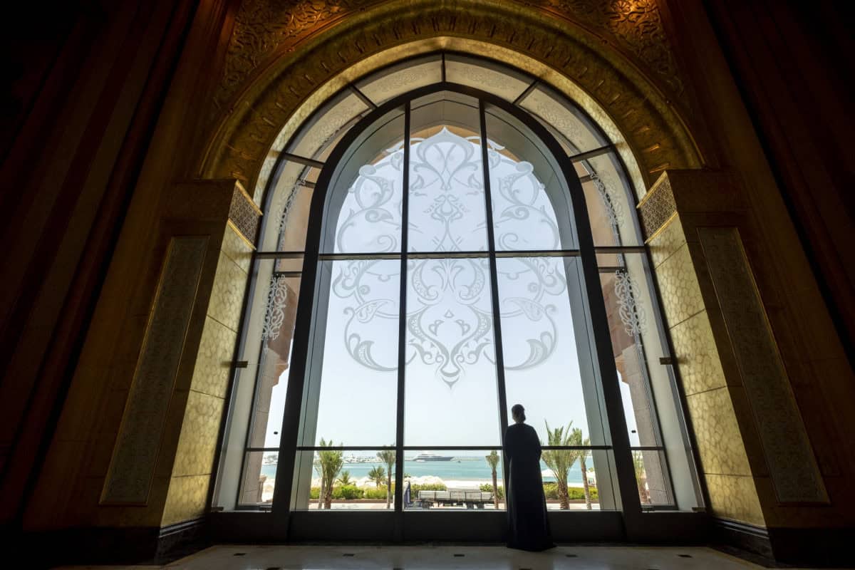Person looking out large arched window with ocean view and decorative design.