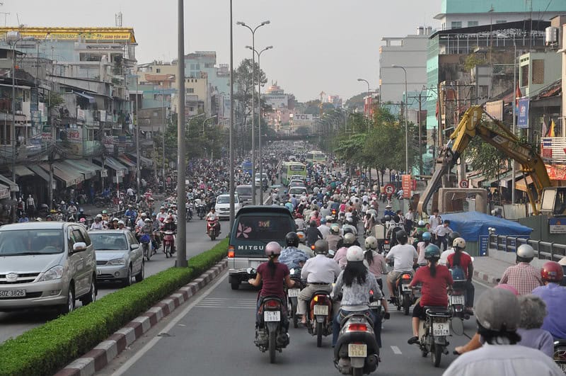 Busy city street with cars and motorcycles in heavy traffic, urban buildings in background.