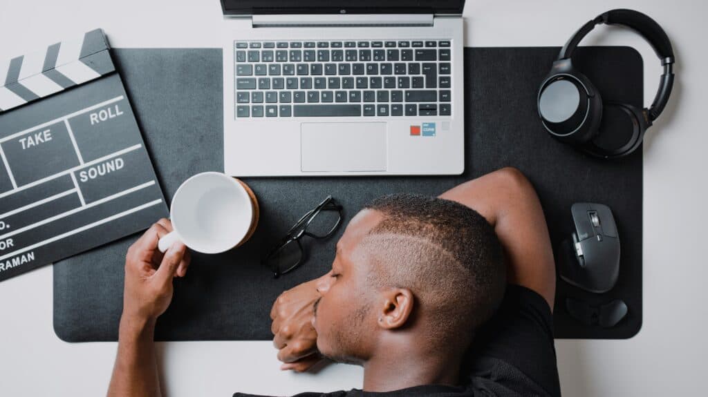 Young man resting at a workspace with laptop, headphones, and film clapperboard.