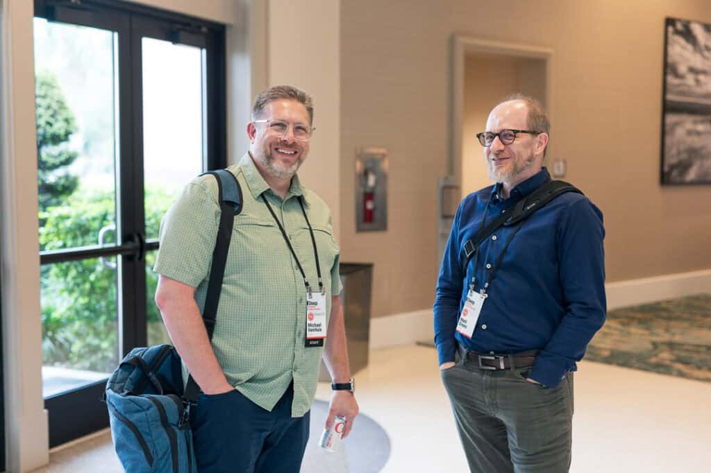 Two men smiling and talking at Missio Nexus conference in a hotel lobby.