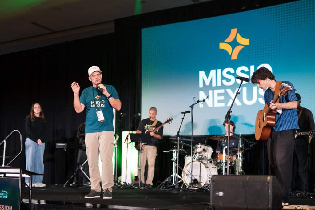 Speakers and musicians at Missio Nexus conference stage with band and large screen.