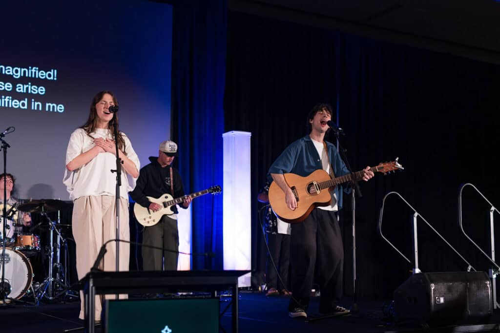 Musicians performing on stage at Missio Nexus conference with guitars and microphones.