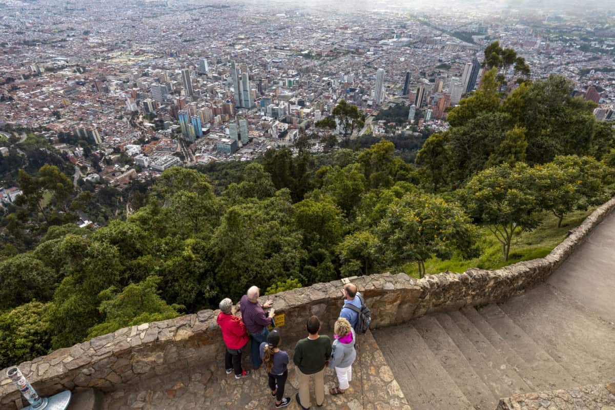 Group of people enjoying a city view from a park overlooking a dense urban area.
