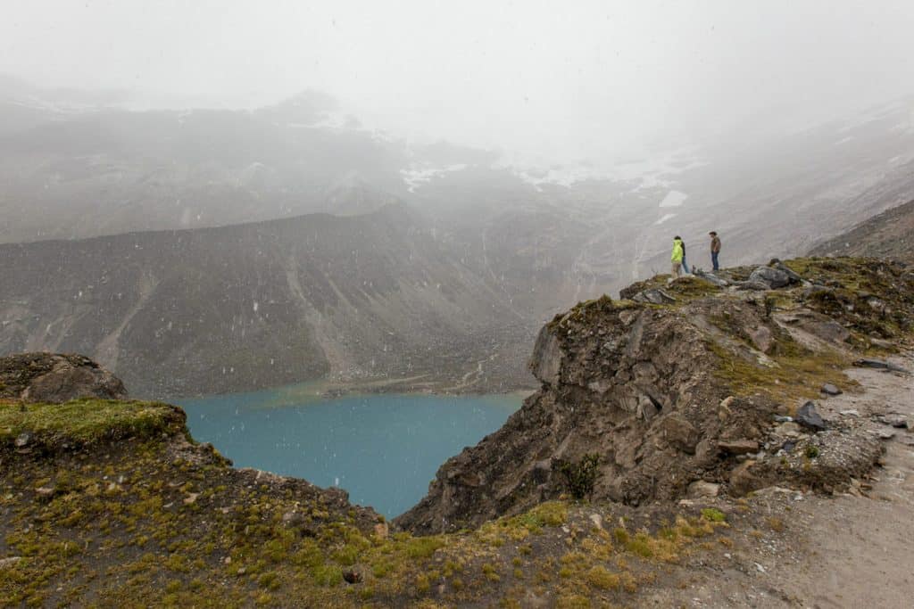 Hikers overlooking a mountain lake in a misty, rugged landscape.