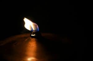 Close-up of a lit candle flame in darkness, symbolizing spirituality and hope.