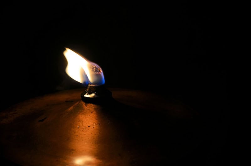 Close-up of a lit candle flame in darkness, symbolizing spirituality and hope.