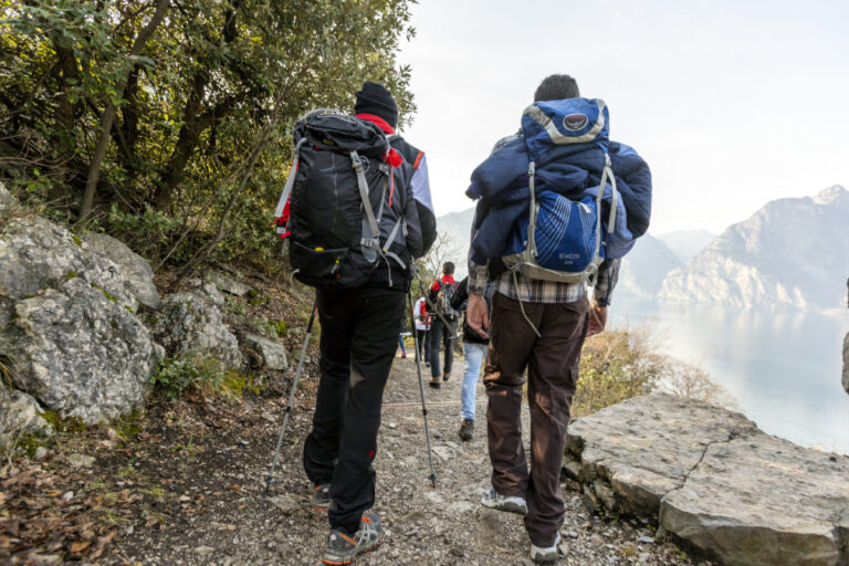 Hikers walking along a scenic mountain trail with backpacks and trekking poles.