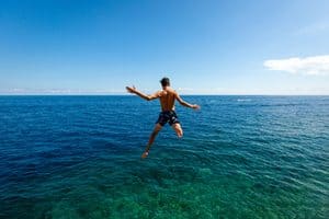 Person jumping into the ocean on a sunny day with clear blue sky.