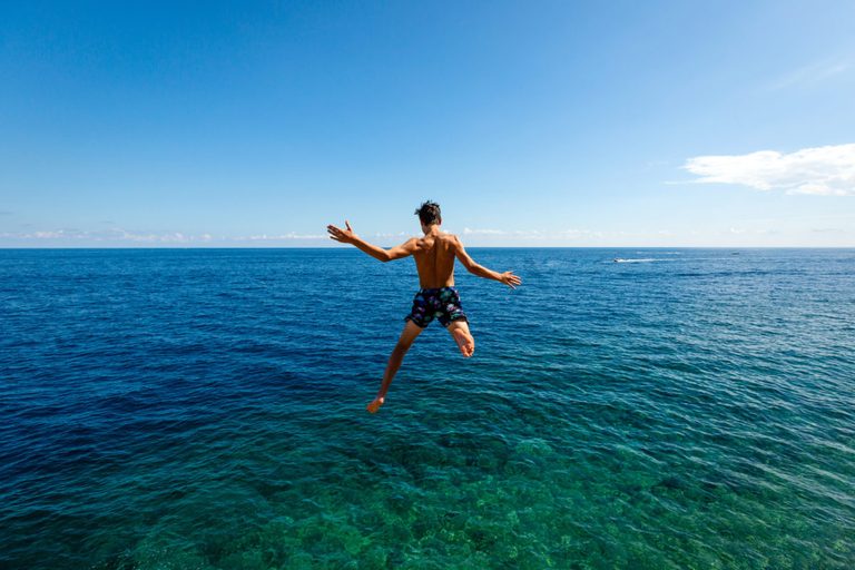 Person jumping into the ocean on a sunny day with clear blue sky.