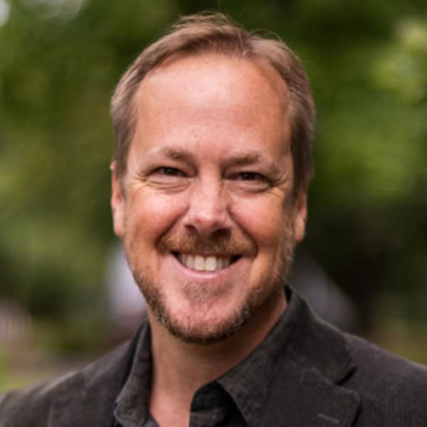Smiling man outdoors with blurred green background.